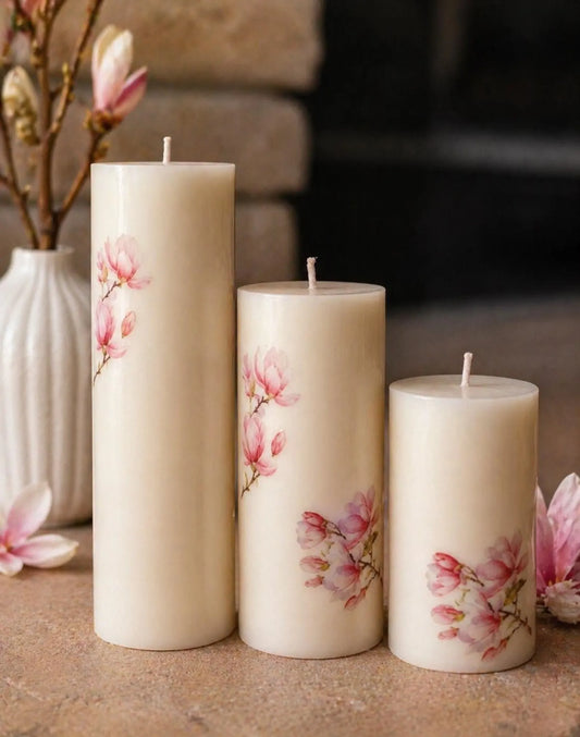 Three decorative candles with floral designs on a surface, with a blurred background.